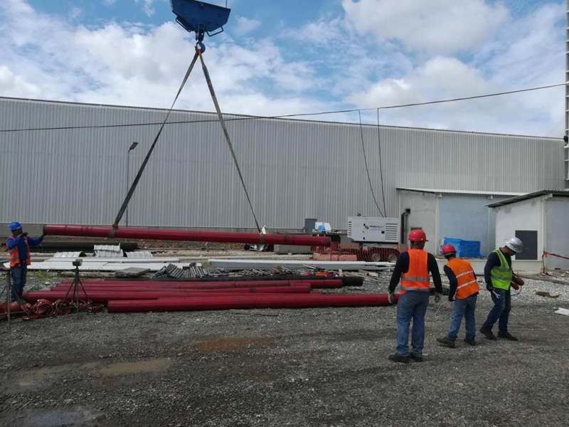 Izaje de tubería roja con grúa en una obra industrial